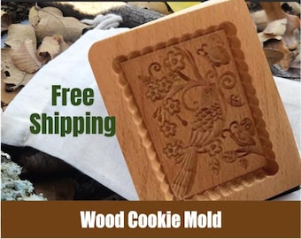 May include: A wooden cookie mold with a detailed design of a bird and flowers. The mold is made of light brown wood and has a rectangular shape.