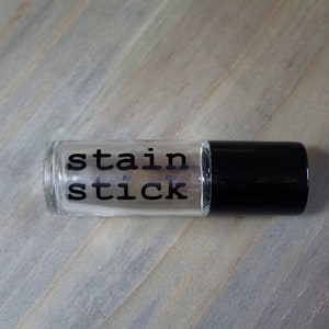 May include: A clear glass bottle with a black cap. The bottle has a label that says "stain stick".