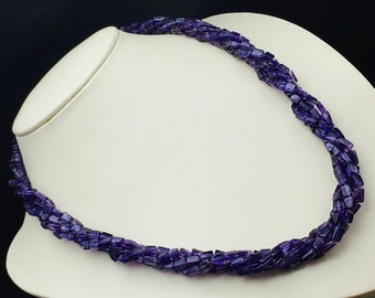 May include: A purple amethyst gemstone necklace with a twisted design. The necklace is made of faceted beads and is displayed on a white mannequin.