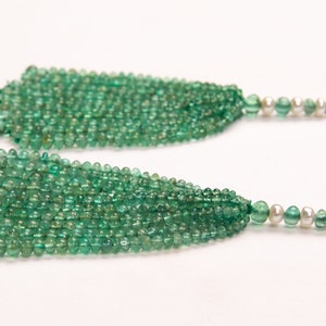 May include: A pair of long, green gemstone earrings with a pearl accent at the end of each earring.