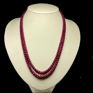 Op de afbeelding: Een dubbele ketting van diep rode robijn kralen. De ketting wordt getoond op een witte mannequinbuste.