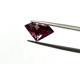 May include: A deep purple gemstone with a square shape is held by tweezers against a white background.