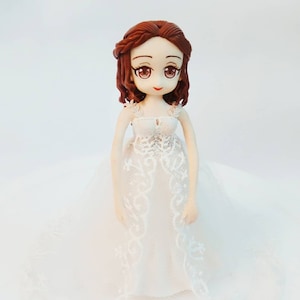 K&ouml;nnte beinhalten: Eine wei&szlig;e Porzellan-Brautpuppe mit braunen Haaren und einem wei&szlig;en Spitzenkleid. Die Puppe hat gro&szlig;e Augen und einen s&uuml;&szlig;en Ausdruck.