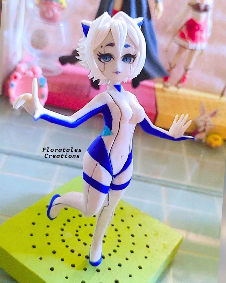K&ouml;nnte beinhalten: Eine wei&szlig;e und blaue Figur einer weiblichen Figur mit Katzenohren. Die Figur ist mit einem erhobenen Bein und dem anderen gebeugten Bein posiert. Die Figur steht auf einem gr&uuml;nen Sockel mit L&ouml;chern.
