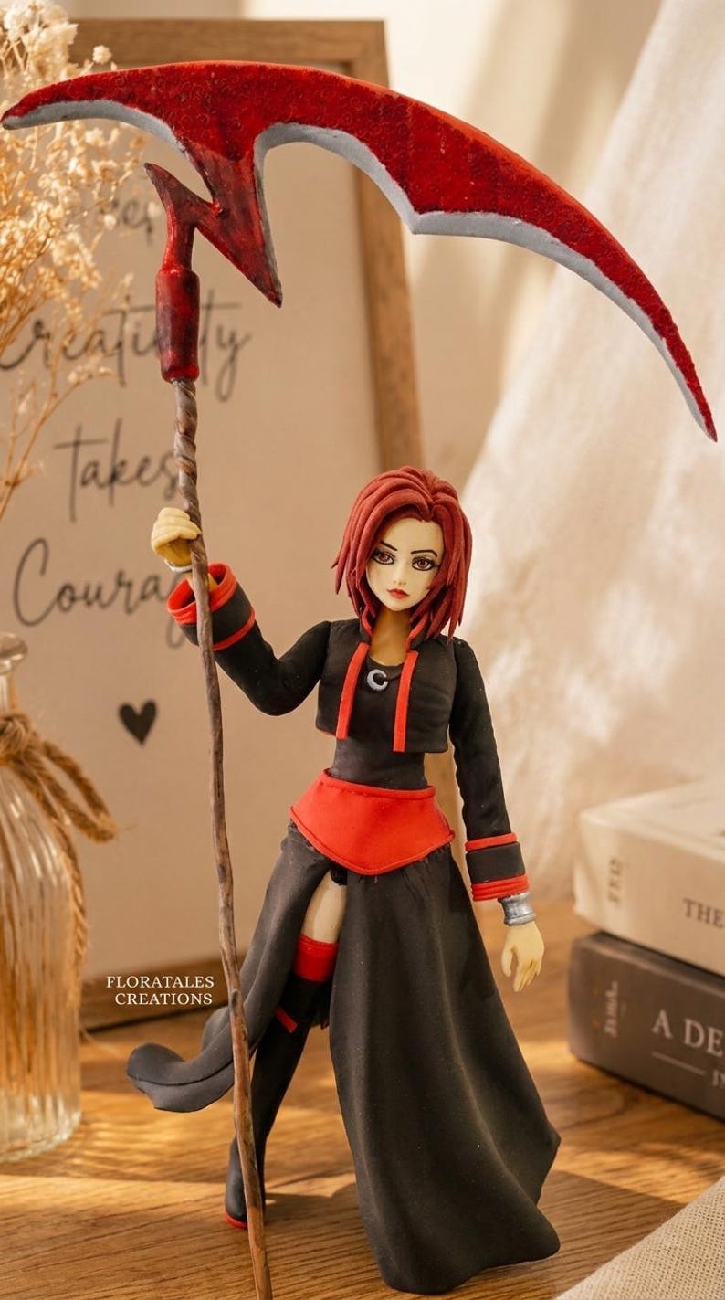 May include: A handcrafted figurine of a character with red hair, wearing a black and red outfit, and holding a red scythe. The figurine is standing in front of a framed print with the text "Creativity takes Courage". The figurine is a Floratales Creation.