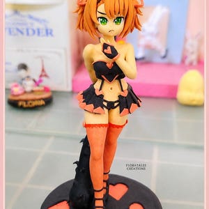 May include: A handcrafted figurine of an anime-style character. The figure has orange hair, green eyes, and is wearing a black and orange outfit. The base is black with orange heart shapes. The figurine is approximately 6 inches tall.