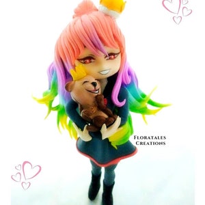 K&ouml;nnte beinhalten: Eine handgefertigte Figur aus Polymer Clay einer jungen Frau mit Regenbogenhaar, die eine Krone tr&auml;gt und einen Teddyb&auml;ren h&auml;lt. Die junge Frau hat rote Augen und ein verschmitztes L&auml;cheln. Der Teddyb&auml;r tr&auml;gt ebenfalls eine Krone.