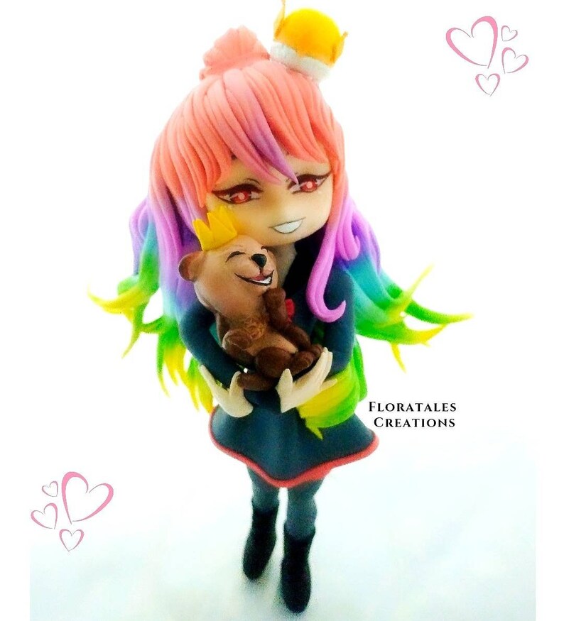 K&ouml;nnte beinhalten: Eine handgefertigte Figur aus Polymer Clay einer jungen Frau mit Regenbogenhaar, die eine Krone tr&auml;gt und einen Teddyb&auml;ren h&auml;lt. Die junge Frau hat rote Augen und ein verschmitztes L&auml;cheln. Der Teddyb&auml;r tr&auml;gt ebenfalls eine Krone.