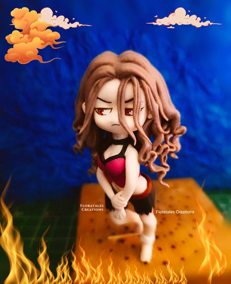 May include: A handcrafted figurine of a female character with long brown hair, red eyes, and a determined expression. She wears a pink and black outfit, posed with a fiery background. The figurine is a unique art piece, with the text "FLORATALES CREATIONS" visible.