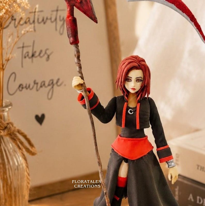 May include: A handcrafted figurine of a female character with red hair, wearing a black outfit with red accents. She holds a staff with a red blade. The background includes text that reads "Creativity takes Courage."
