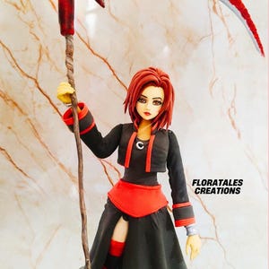 May include: A handcrafted figurine of a character holding a red scythe. The figure wears a black outfit with red accents and has red hair. The text "FLORATALES CREATIONS" is visible.