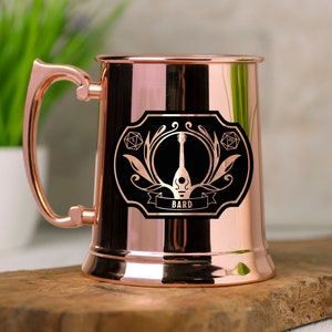 Puede incluir: Taza de cobre con un diseño en blanco y negro de un laúd y la palabra "BARD".
