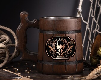 May include: A dark brown wooden beer mug with a decorative handle. The mug features a black and copper emblem with the word "PALADIN". The mug has a stainless steel interior and is banded with black trim.