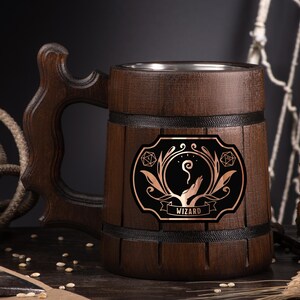 May include: A dark brown wooden beer mug with a decorative handle. The mug features a black and copper emblem with the word "WIZARD" on it. The mug has a stainless steel interior and is designed for beverages.