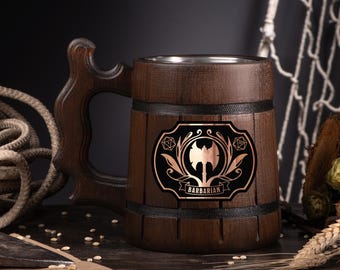 May include: A dark brown wooden beer mug with a decorative handle. The mug features a black and copper emblem with an axe and the word "BARBARIAN". The mug has a stainless steel interior and is banded with black trim.