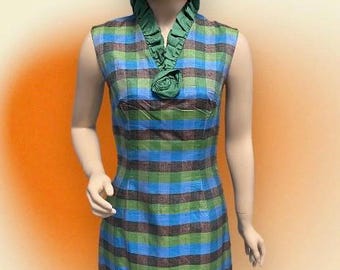 Puede incluir: Un vestido sin mangas con estampado de cuadros verdes y azules. El vestido tiene un cuello con volantes y un acento de rosa verde. El vestido es entallado y tiene una longitud corta.