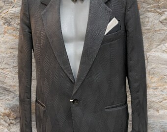 May include: A black patterned blazer with a floral bow tie and a white pocket square. The blazer has a single button closure and a notched lapel.