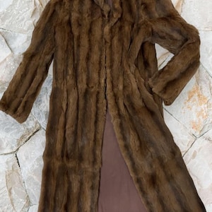 Könnte beinhalten: Ein langer brauner Pelzmantel mit gerader Schnittführung und einem vorderen Mittelverschluss. Der Mantel ist aus weichem, luxuriösem Pelz gefertigt und hat einen klassischen, zeitlosen Stil.