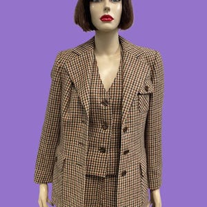 May include: A three-piece suit featuring a blazer, waistcoat, and trousers in a brown, black, and white houndstooth pattern. The blazer has notched lapels, long sleeves, and two front flap pockets. The waistcoat includes a button-down front closure.