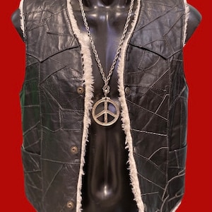 Può includere: Un giubbotto di pelle nera con un colletto di pelliccia bianca e una collana con un ciondolo a forma di segno della pace argentato.