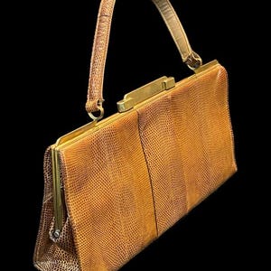 Op de afbeelding: Een vintage, rechthoekige handtas in een warme, goudbruine tint. De tas heeft een textuur met reptielachtig patroon, een gestructureerd frame en een bijpassende handgreep. De hardware is glanzend goudkleurig en voegt een vleugje elegantie toe aan dit klassieke accessoire.