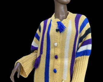May include: A long yellow striped cardigan with purple, blue, white, and black stripes. The cardigan has a button closure and tassels on the front.