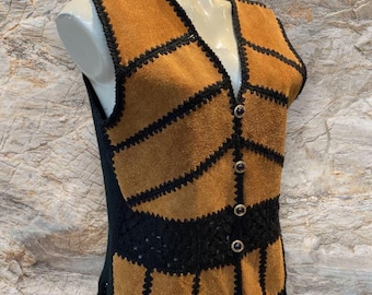 May include: A vintage patchwork vest in tan and black. The vest has tan suede panels with black stitching, a V-neck, decorative buttons, and a fringed hem. It is displayed on a mannequin.
