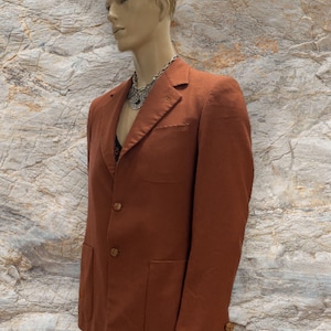 May include: A rust-colored blazer with three buttons and two patch pockets. The blazer has a notched lapel and a single button on each cuff.