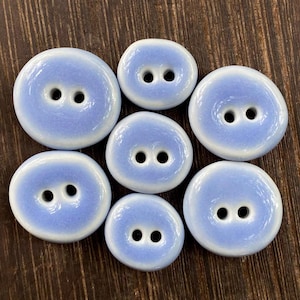 May include: Set of eight ceramic buttons in a light blue and white colour scheme. The buttons are oval shaped with two holes each.