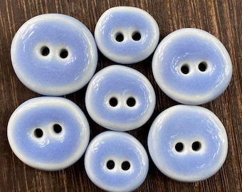 May include: Set of eight ceramic buttons in a light blue and white color scheme. The buttons are oval shaped with two holes each.