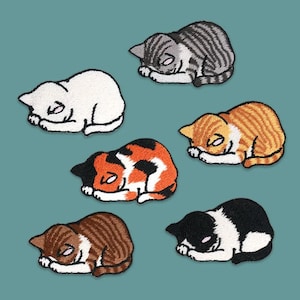 Op de afbeelding: Zes geborduurde strijkpatches van slapende katten in verschillende kleuren en patronen. De katten liggen opgerold met hun poten onder hun kin.