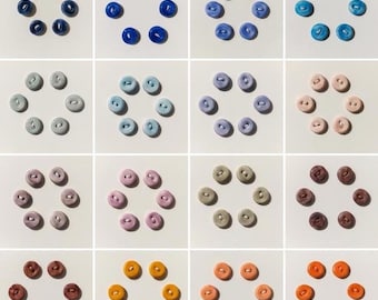 May include: A grid of colorful buttons arranged in circular patterns. The buttons are in various shades, including green, blue, purple, pink, orange, and brown. Each button has two or four holes. The buttons are on a white background.