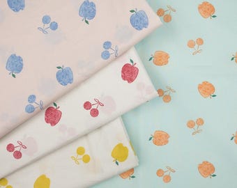 May include: Four fabric swatches with different fruit patterns. The top swatch is pink with blue apples and cherries. The second swatch is white with red apples and cherries. The third swatch is white with yellow apples and cherries. The bottom swatch is light blue with orange apples and cherries.