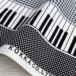 Könnte beinhalten: Schwarz-weißes Stoffmuster mit sich wiederholenden Klaviertasten, Punkten und Karos. Der Stoff trägt den Aufdruck "KOKKA CO., LTD.".
