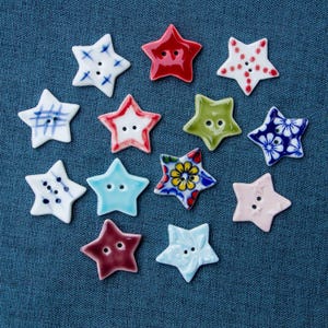 Puede incluir: Una colección de 12 botones de cerámica en forma de estrella en varios colores y patrones. Los botones presentan diferentes diseños, incluyendo patrones florales, geométricos y abstractos.