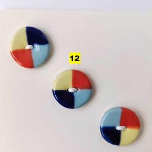 May include: Three colorful, round buttons with a four-sectioned design in red, yellow, blue, and light blue. Each button has a white center with two holes for sewing. The number "12" is in a yellow square.