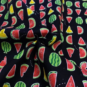 May include: Black fabric with a repeating pattern of watermelon slices and whole watermelons. The watermelons are red, green, and yellow.