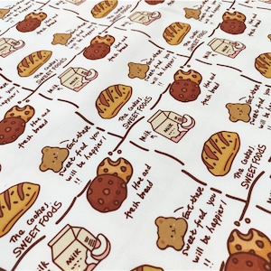 Op de afbeelding: Witte stof met een herhalend patroon van bruine en witte koekjes, brood, melkpakken en beren. De tekst "The Cookies: Sweet Foods" wordt herhaald in het hele patroon.