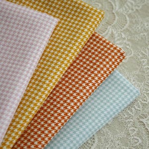 May include: A collection of folded fabric swatches in various colors, including pink, yellow, orange, and blue. Each swatch features a classic houndstooth pattern in white. The fabrics are arranged in a fan shape, showcasing the different color options.