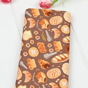 May include: Brown fabric with a repeating pattern of various breads, pastries, and a cat with the text "cocoa bakery" on it.