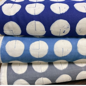 Könnte beinhalten: Drei Rollen Stoff mit einem weißen Polka-Dot-Muster auf blauem Hintergrund. Der Stoff ist gefaltet und übereinander gestapelt. Die obere Rolle ist dunkelblau, die mittlere Rolle ist hellblau und die untere Rolle ist graublau.