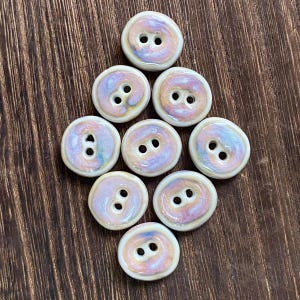 May include: Eight ceramic buttons with a white base and a swirl of pink, purple, and brown. The buttons have two holes each.