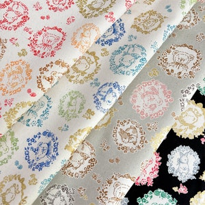May include: Two pieces of fabric with a white background and a repeating pattern of animals in circles. The animals are in shades of brown, pink, and blue. The fabric is folded over itself, showing the pattern on both sides.
