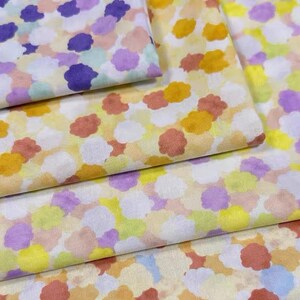 Könnte beinhalten: Ein Stapel Stoff mit weißem Hintergrund und einem bunten Muster aus kleinen, abstrakten Formen in Gelb-, Orange-, Lila- und Blautönen.
