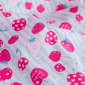 May include: A blue and white striped fabric with a repeating pattern of pink cherries, strawberries, and apples. The fabric has the words "cherries", "apples", "We love fruits", and "It's time to smile" printed on it.