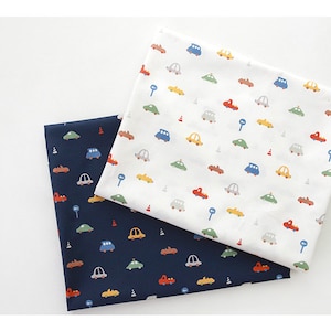 May include: Two fabric swatches with a repeating pattern of colorful cars, traffic cones, and street signs. One swatch is white with a light blue background and the other is navy blue with a white background.