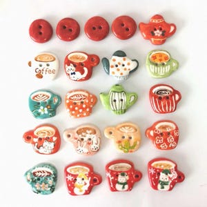 May include: A collection of decorative ceramic buttons in various shapes and colors. The buttons include red circles, teapots, and coffee cups with detailed designs. Some cups have the word "Coffee" on them.