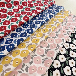 May include: Five folded pieces of fabric featuring a repeating floral pattern. The prints include red, blue, yellow, pink, and white flowers with green or gray leaves on white or black backgrounds, showcasing a consistent stylized botanical design.