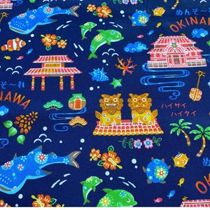 May include: Navy blue fabric with a repeating pattern of Okinawa-themed illustrations. The design includes whales, dolphins, traditional buildings, flowers, and text in Japanese. The overall theme is a vibrant and colorful depiction of Okinawan culture.