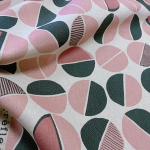 Könnte beinhalten: Ein Stoff mit einem sich wiederholenden Muster aus rosa und grünen Halbkreisen. Der Stoff hat einen weißen Hintergrund.